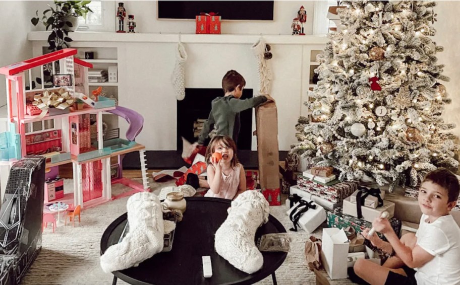 kids opening gifts in living room on christmas morning with barbie house and stockings