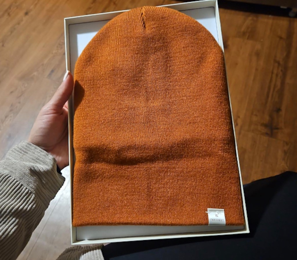 hand holding orange beanie in box