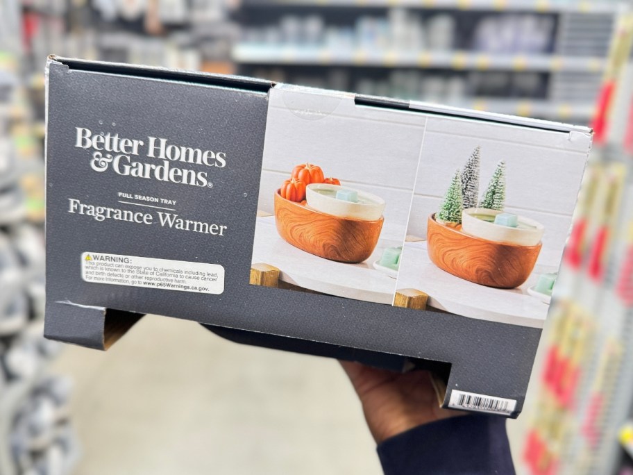 hand holding a wax warmer with a wood look base and decorative pumpkins and trees in the box at Walmart