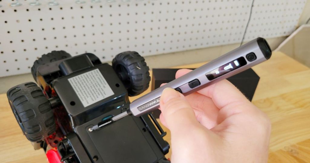 Hand holding an electric screwdriver and using it on a toy truck
