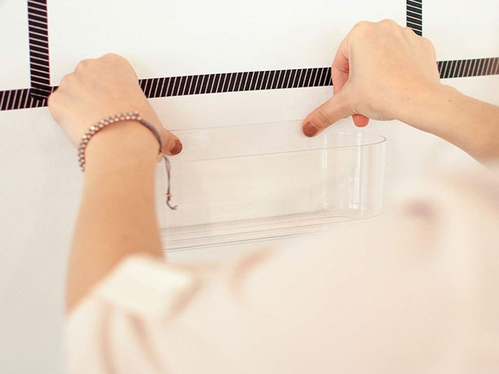 person sticking plastic caddy onto wall