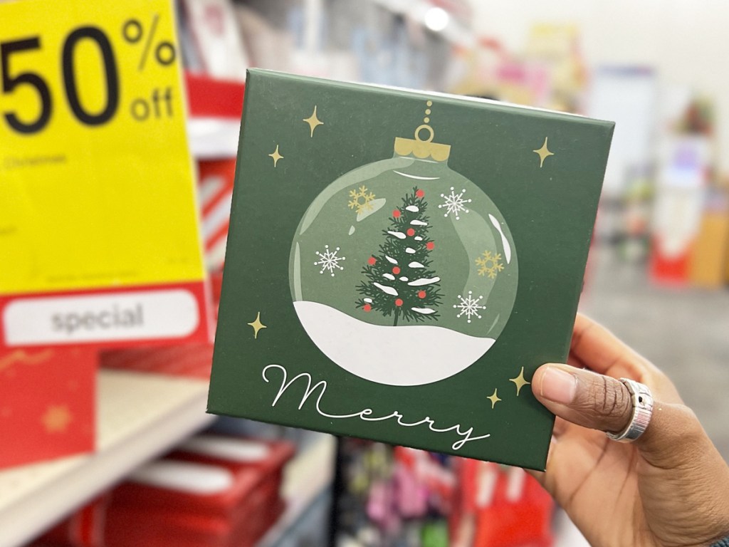 hand holding up a green sign that says merry with an ornament on it