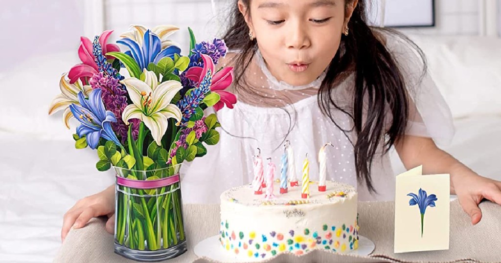 Paper flower bouquet with little girl blowing candle on birthday cake