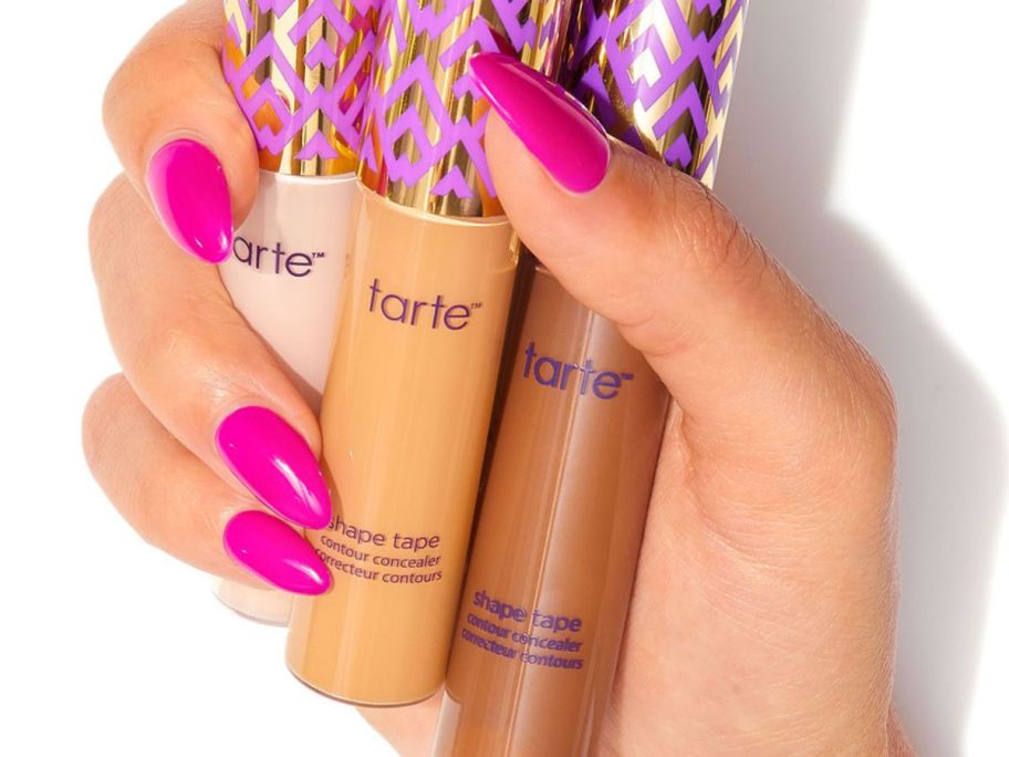 Hand holding three tubes of Tarte Shape Tape concealer.