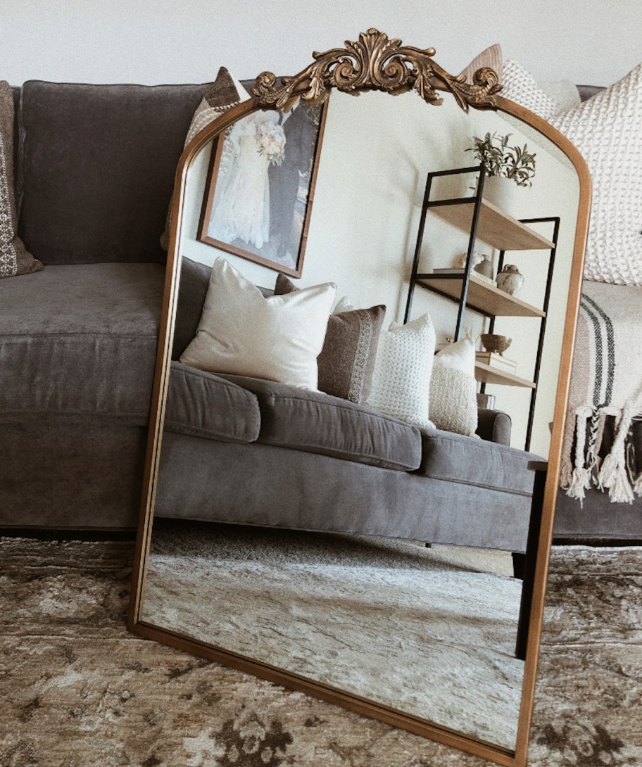 gold mirror on rug leaning on gray couch 
