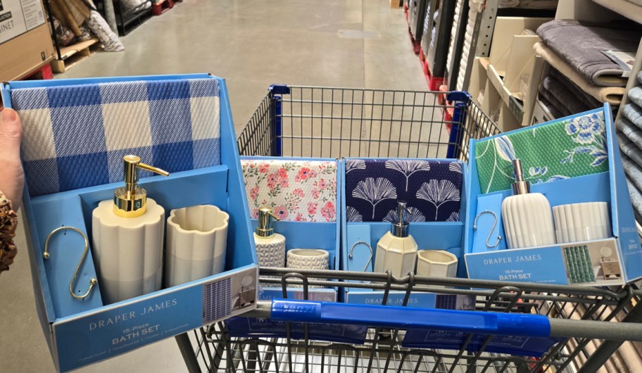 hand holding a 15 piece draper and james bathroom set with other sets displayed inside of a sams club shopping cart