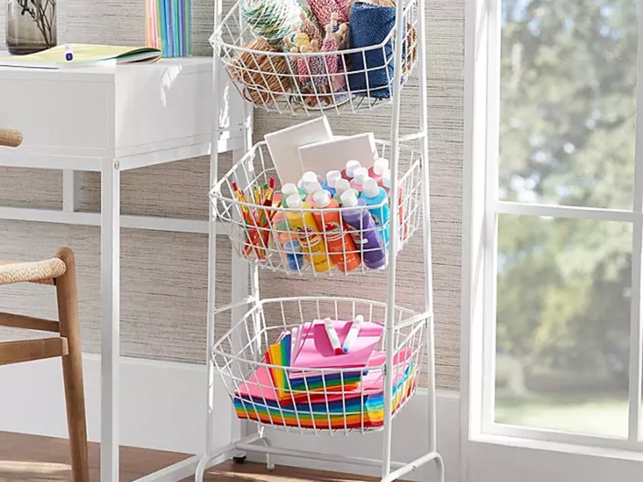 white 3 tier basket stand full of art supplies next to desk 