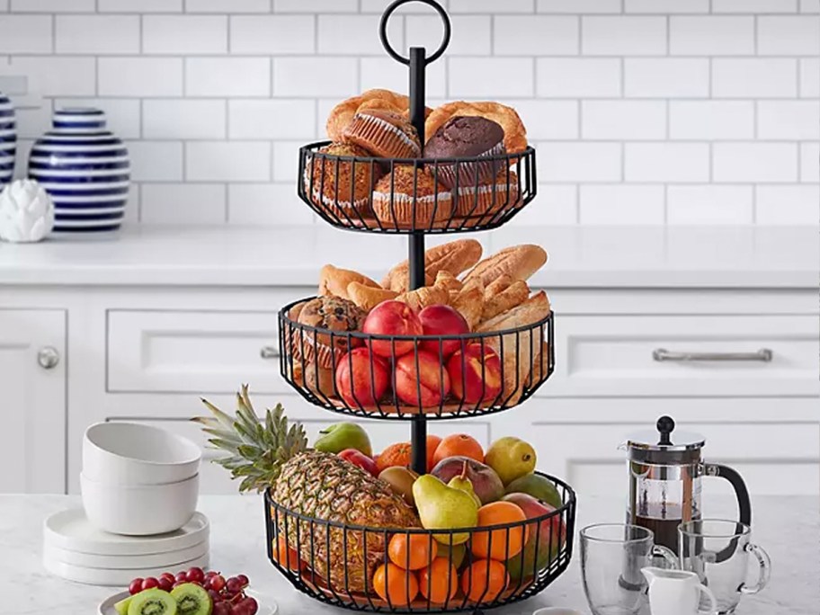 3 tier wire baskets full of fruit and muffins on counter