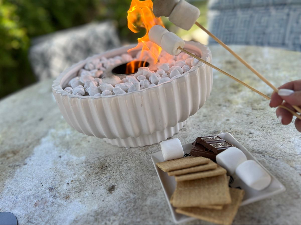 white planter with with decorative stones and mini fire pit in middle with person roasing marshmallows