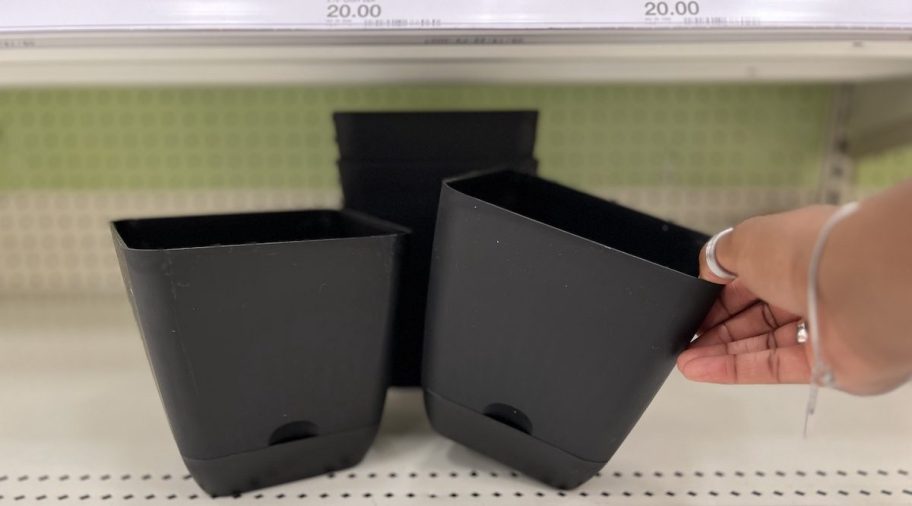 hand grabbing one black self watering planters on store shelf