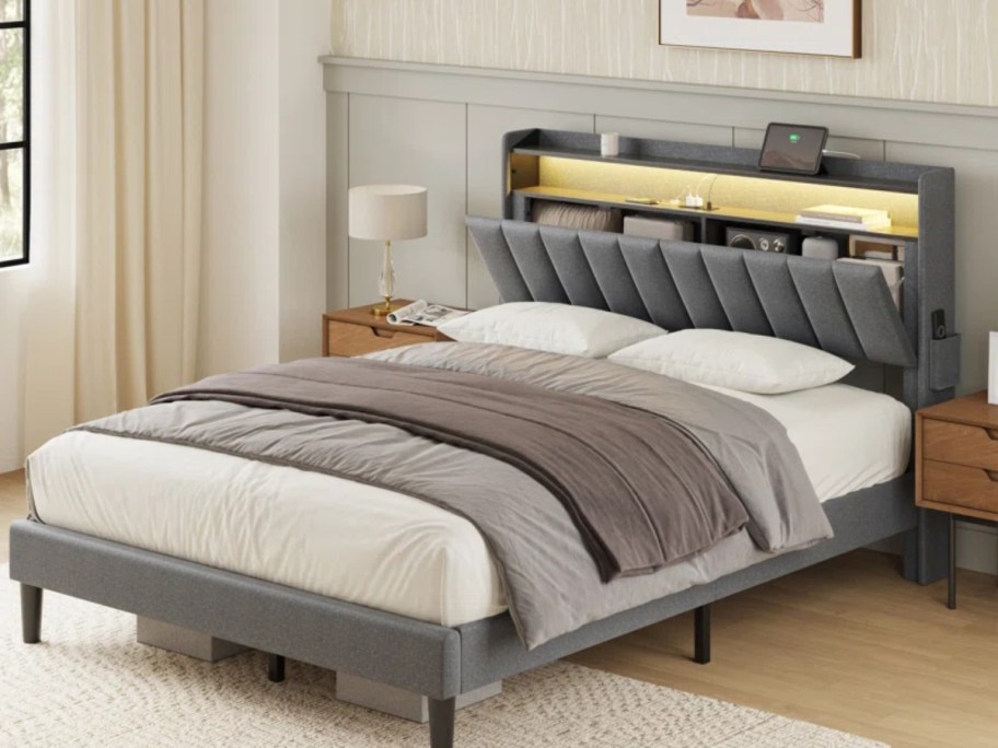 grey upholstered platform bed with headboard that tilts down to reveal a storage area 