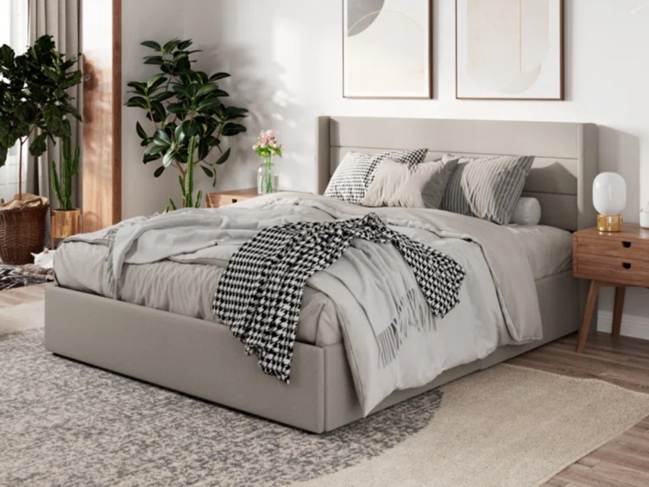 light grey upholstered platform bedrame and headboard that lifts up for storage underneath with matching bedding on it in a room