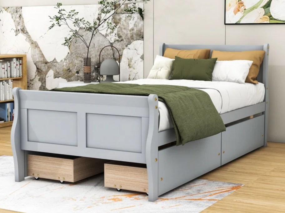 grey wood platform bed frame with headboard and storage drawers underneath with bedding on it in a bedroom