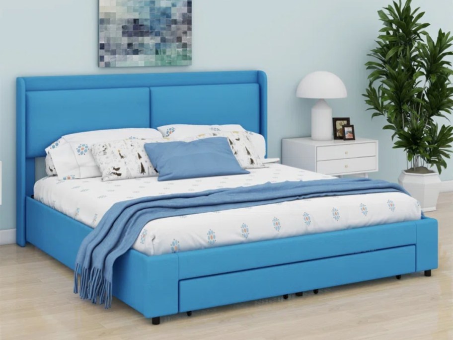 queen size bed with bright blue platform frame and headboard and storage drawer with bedding on it in a room