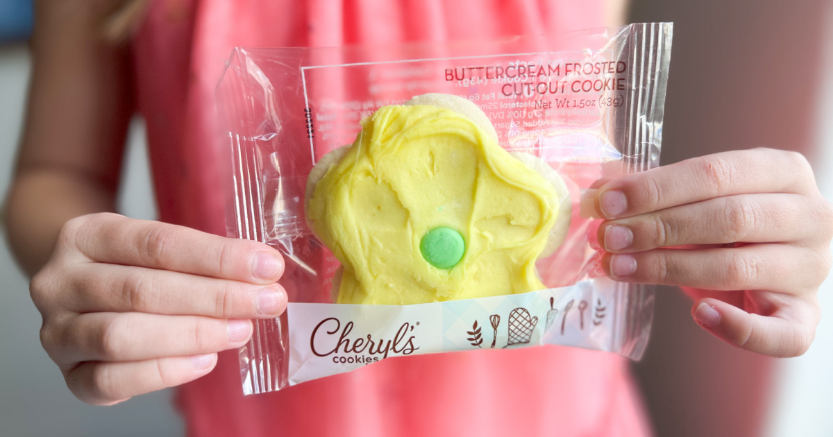 person in a pink shirt holding up a flower shaped cheryl's cookie in packaging