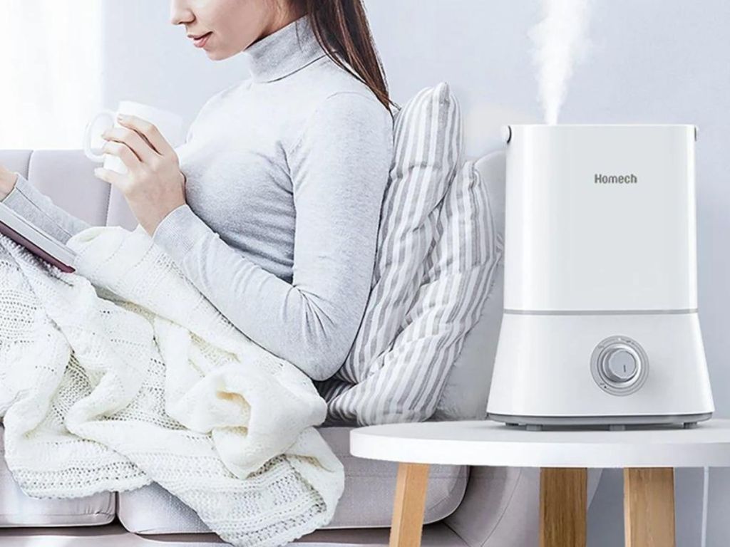 Woman reading book on couch and drinking from a mug with a humidifier running on a table nearby