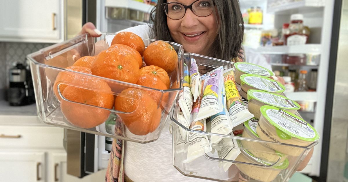 woman holding clear bin filled with oranges in one hand and clear bin filled with snacks in the other hand