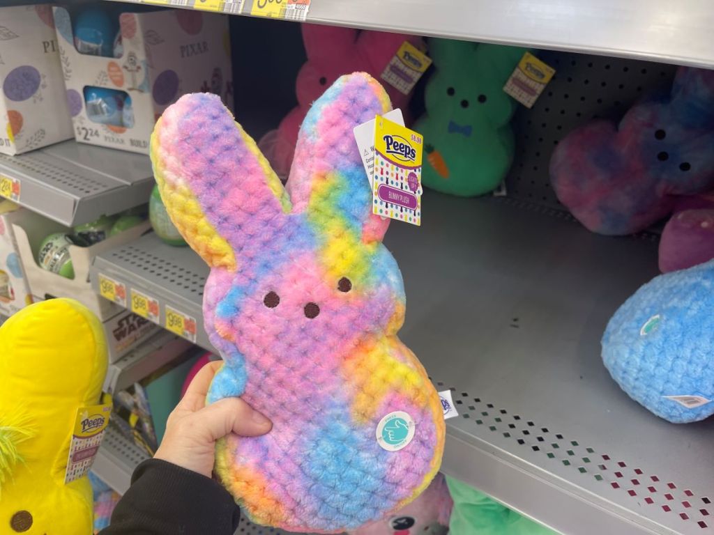 Hand holding a tie-dye plush Peep bunny in front of a shelf at a store