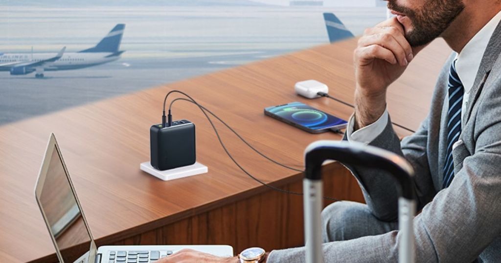 black 4-port charger with phone nad earbuds plugged into it and man working on laptop