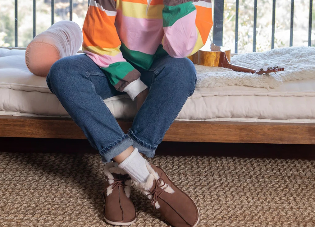 Woman sitting on a bench wearing Rocket Dog boots, jeans and a multicolor tee