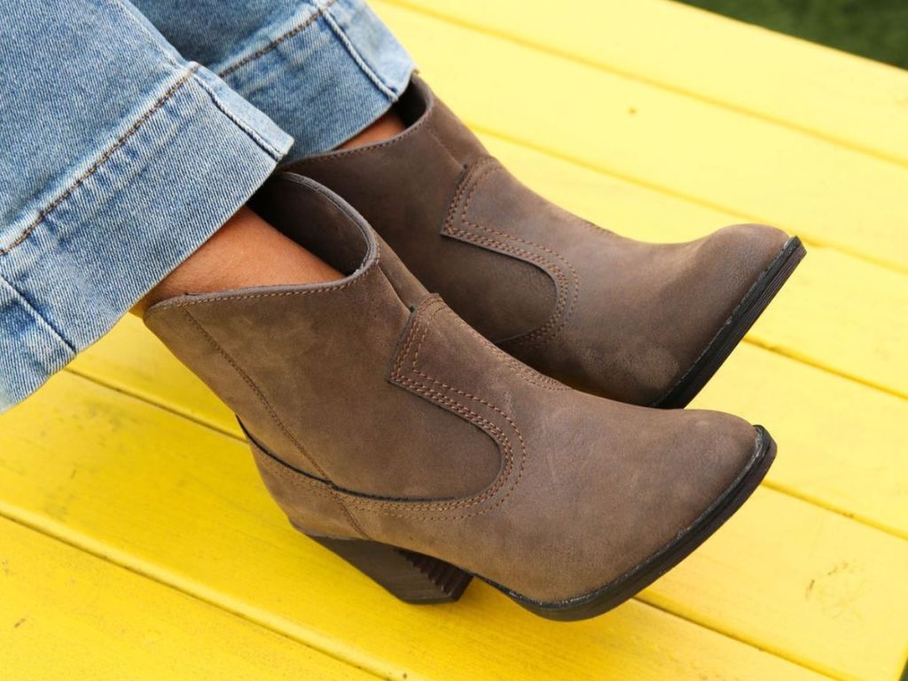 Person wearing a pair of brown Rocket Dog boots and sitting on a bright yellow table