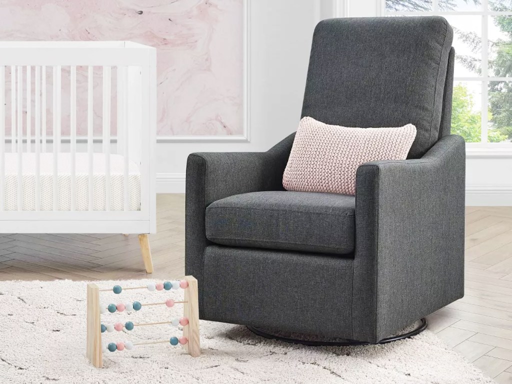 grey rocking chair with a light pink throw pillow in a nursery