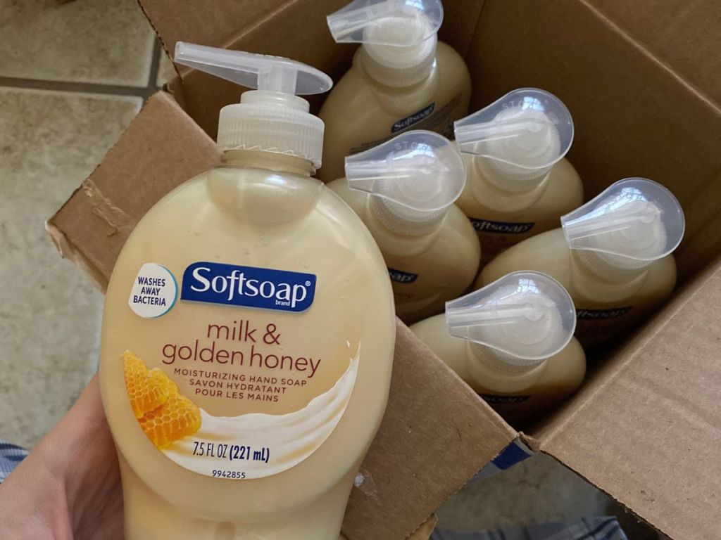 Hand holding a bottle of Softsoap Milk & Honey Soap in front of a box of 5 more