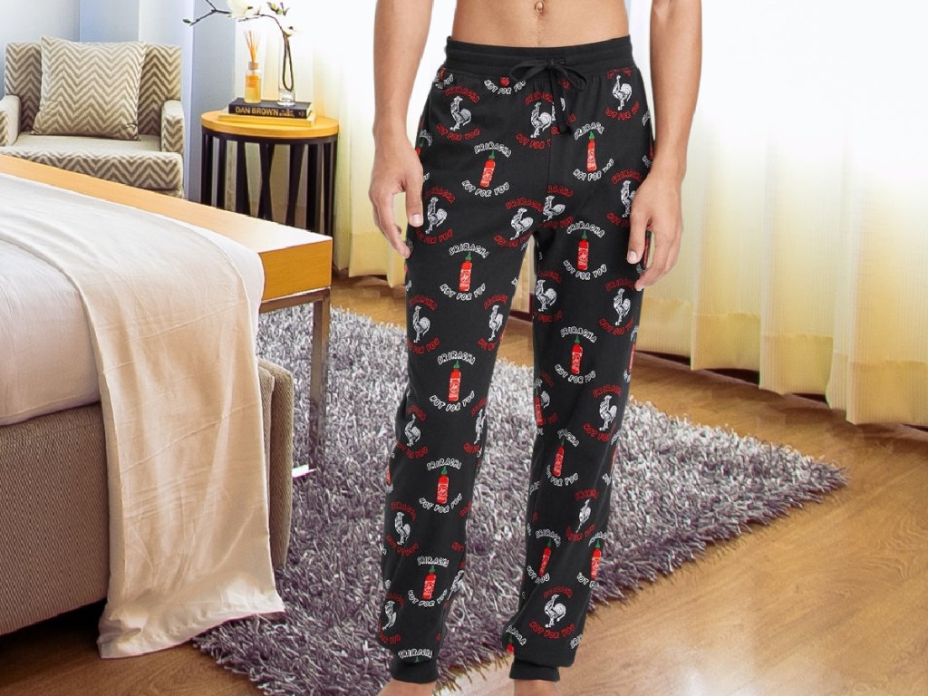 Man wearing Sriracha pajama pants standing next to a bed