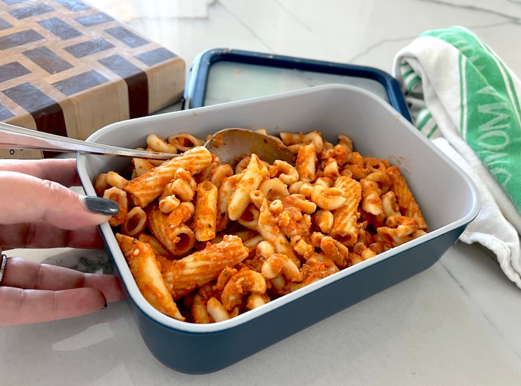 hand holding navy colored dish filled with leftover pasta