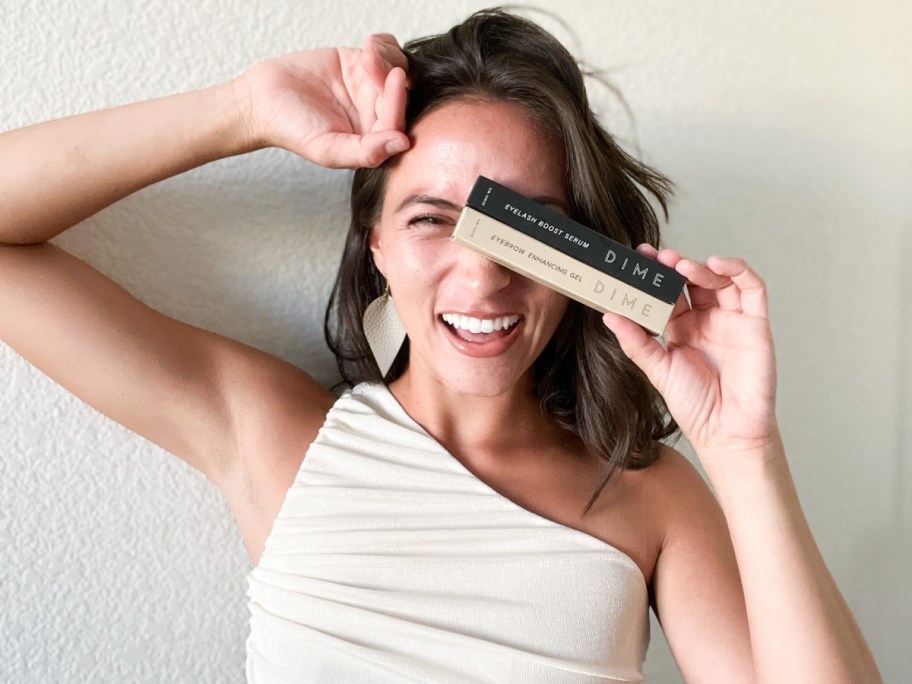 woman holding to mascaras over eye