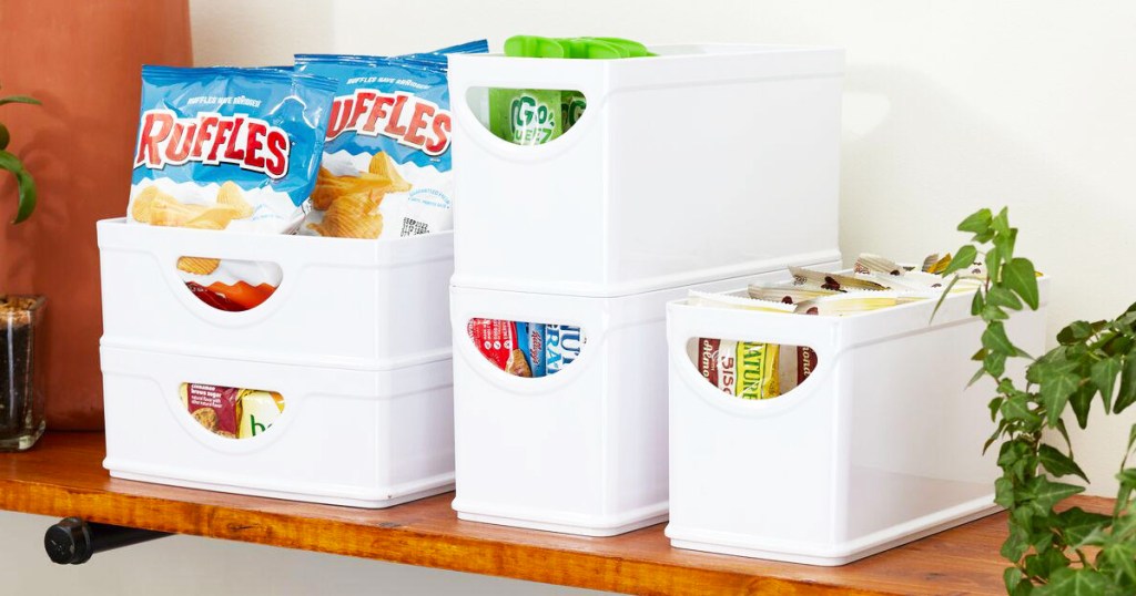 5 white storage bins with food and drinks inside on a wood shelf