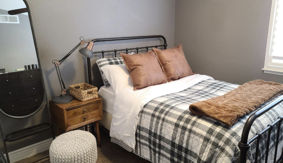 bedroom with full size bed and plaid comforter with leather pillows and lamp