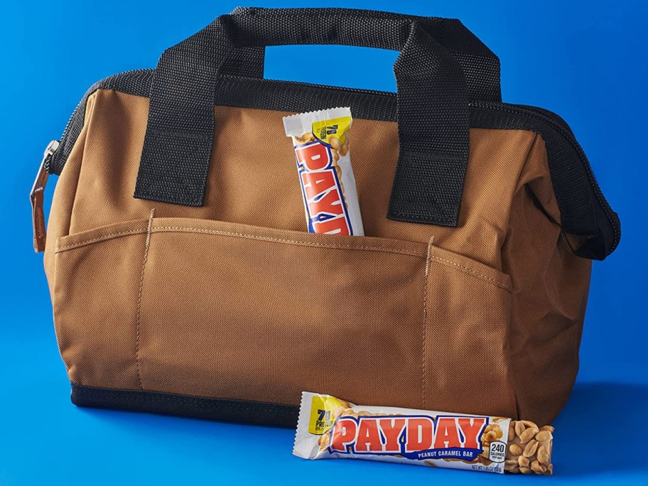 work satchel with a payday candy bar tucked into the front pocket and one sitting in front of it