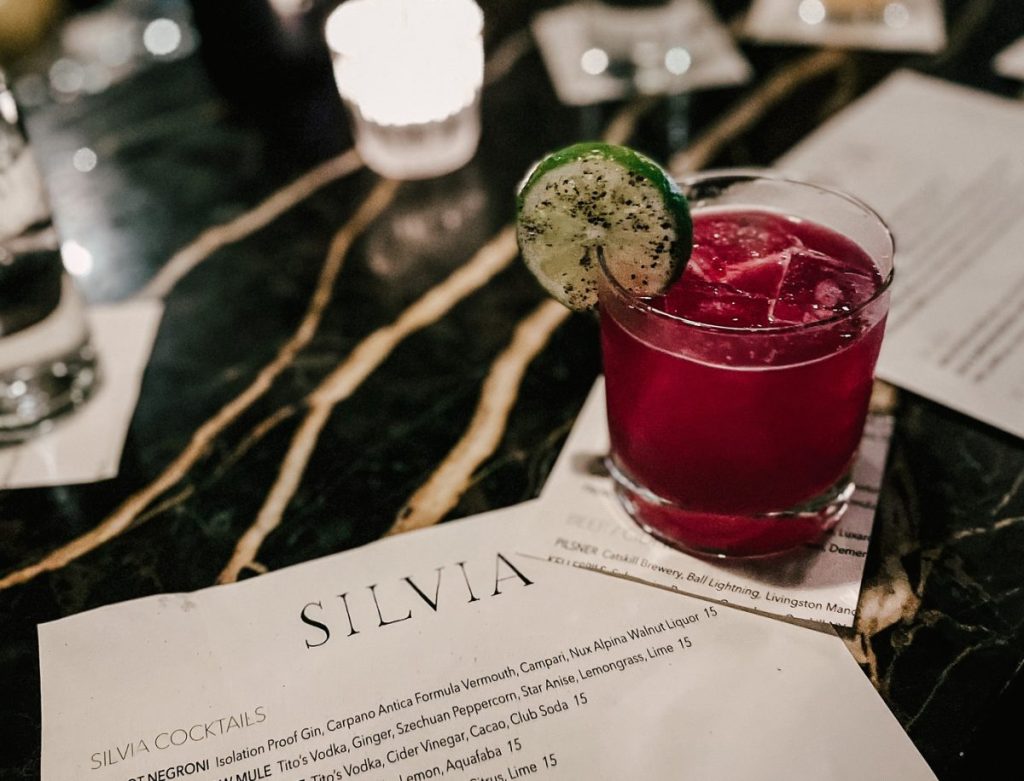 red cocktail with lime on bar with drink menu