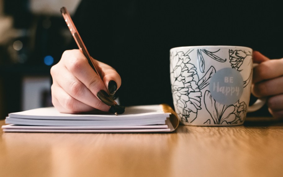 woman writing and holding a cup of coffee