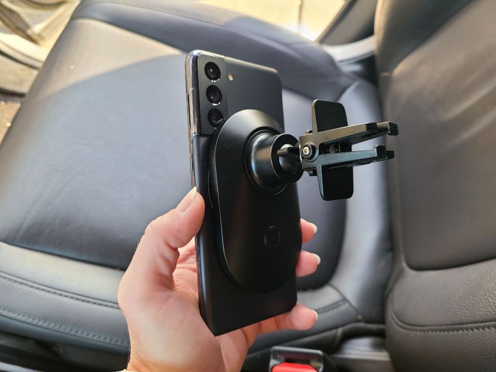 hand holding smartphone car vent mount with leather driver seat in background