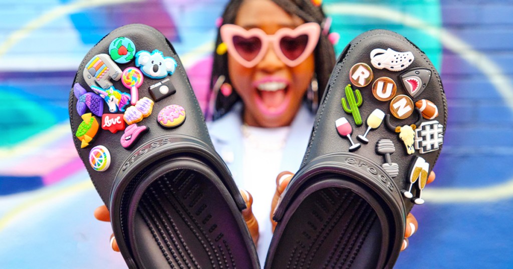 woman holding up a pair of black crocs covered in jibbitz charms