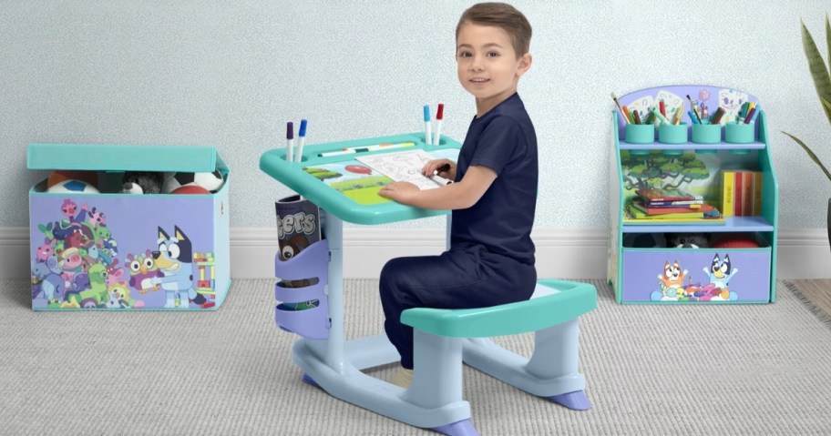 little boy siting at a Bluey art desk with markers and paper, Bluey toy box and art storage center in the background