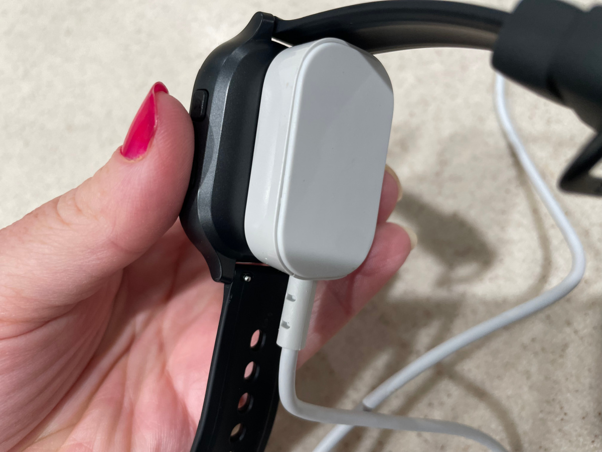 A woman holding a Gabb watch with corresponding charger