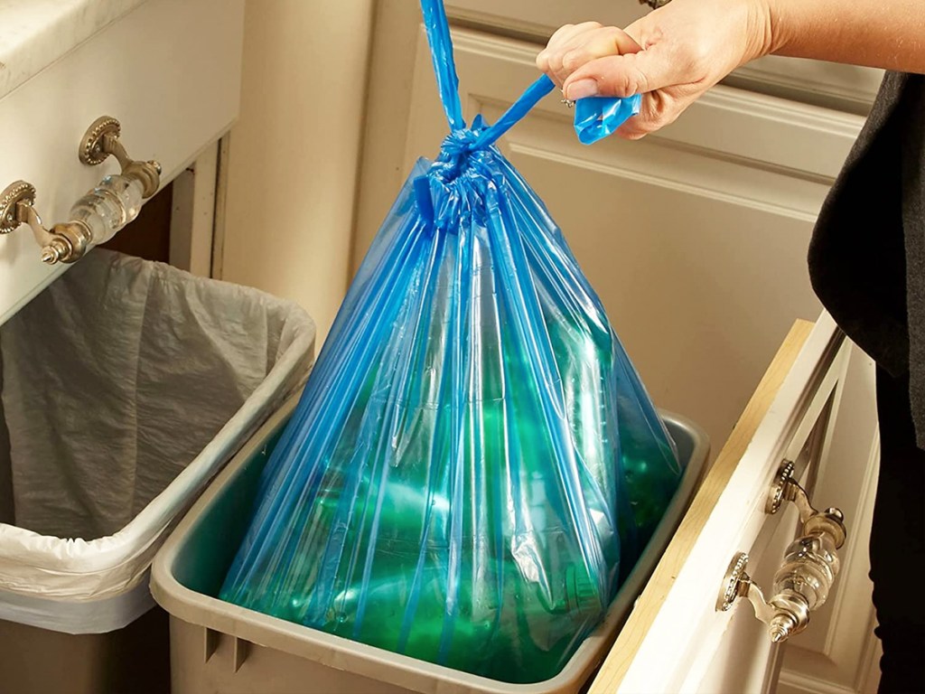 tying knot in blue trash bag with empty bottles inside