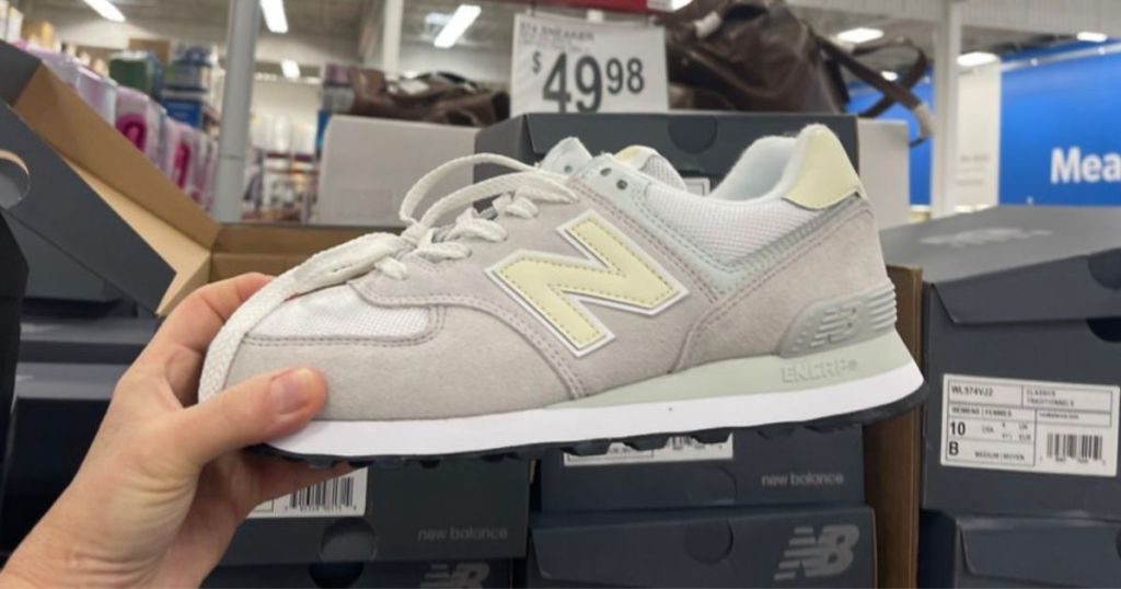 hand holding light gray, white, and light yellow New Balance sneaker in store
