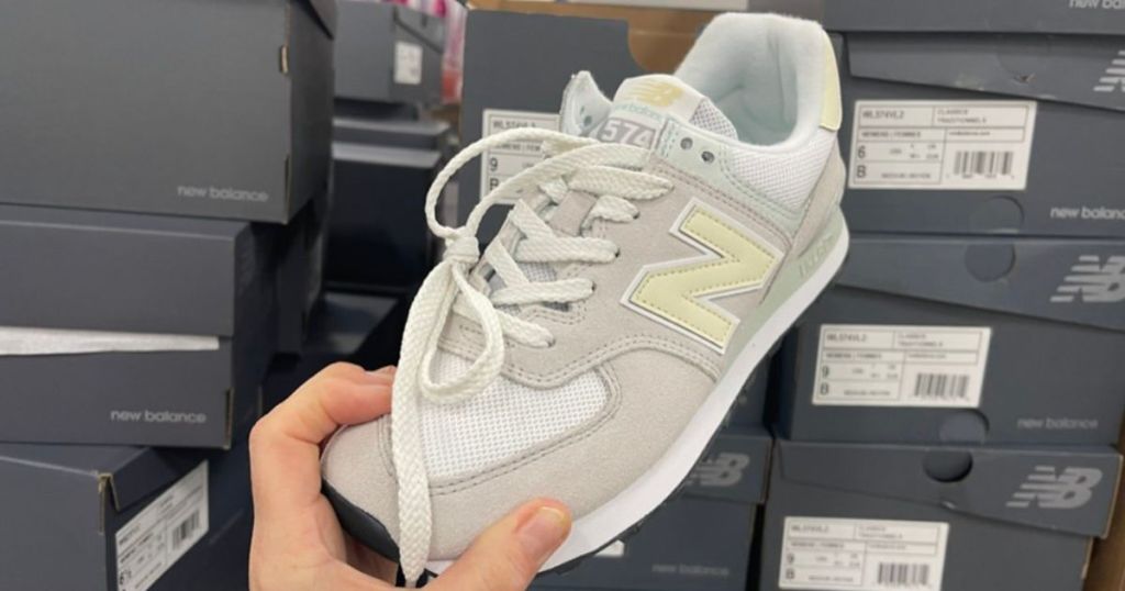 hand holding light gray, white, and light yellow New Balance sneaker in store