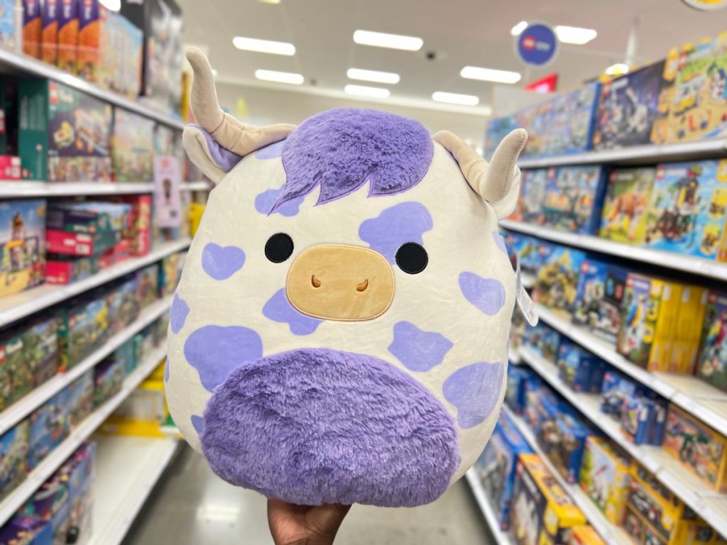 person holding Squishmallows 16" Conway the Purple Spotted Highland Cow Plush Toy