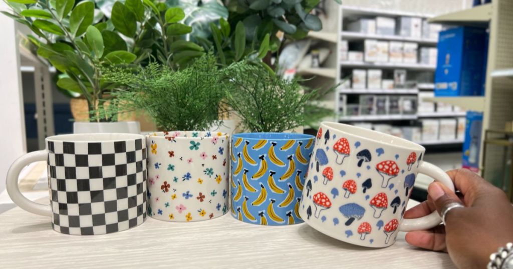 4 coffee mugs on a table with a hand grabbing one of them