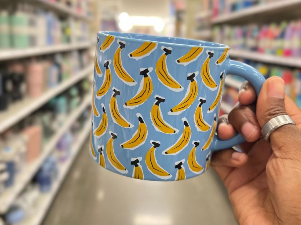 a white mug with bananas on it being held by a hand in a grocery store