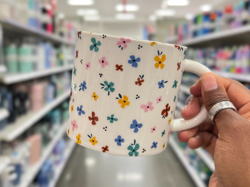 a white mug with flowers on it being held by a hand in a grocery store