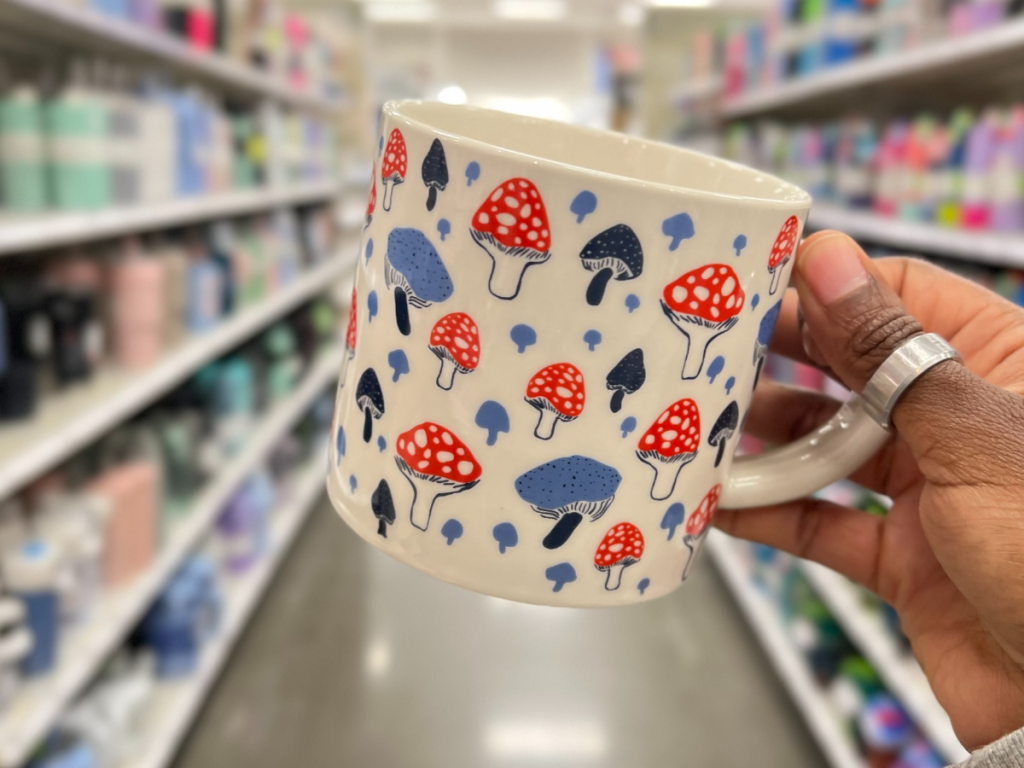 A white mug with mushrooms on it being held by a hand in a grocery store