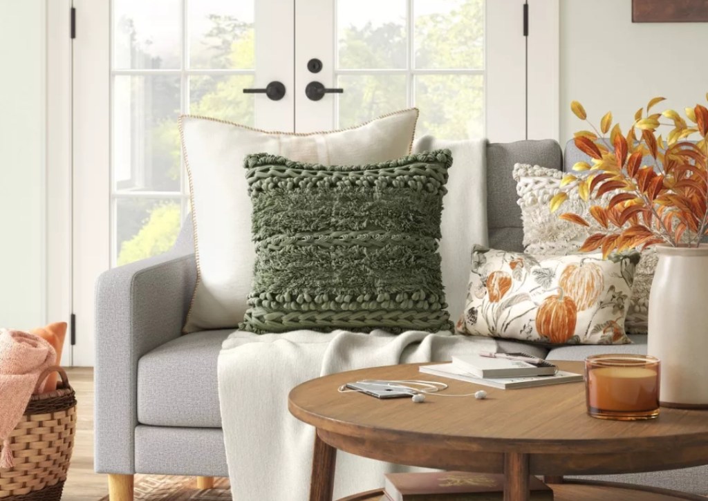 Pillows on a couch and a coffee table in front of it with a magazine, candle, and vase