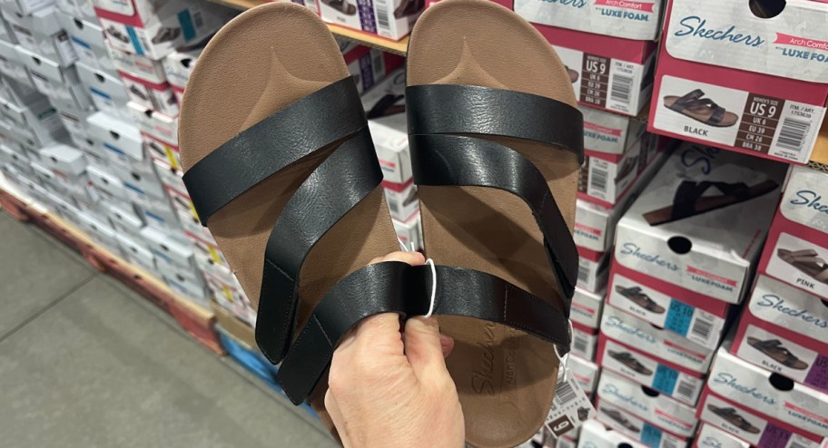 woman holding a pair of black skechers sandals