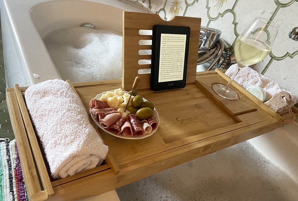 bathtub tray with towel, snacks, and kindle over a tub